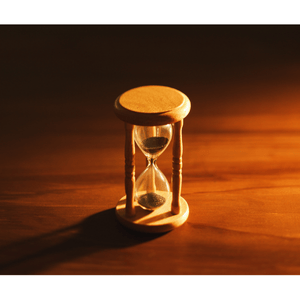 Wooden hourglass glowing in warm light on a wooden table, symbolizing time passing and the importance of taking action now.